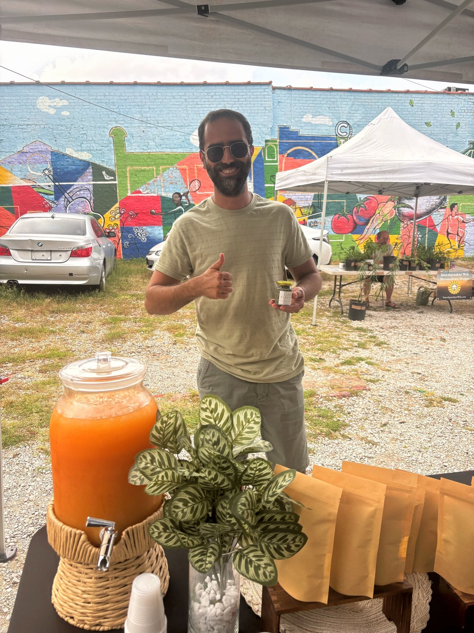 Man giving a thumbs up at an outdoor event with a colorful mural in the background