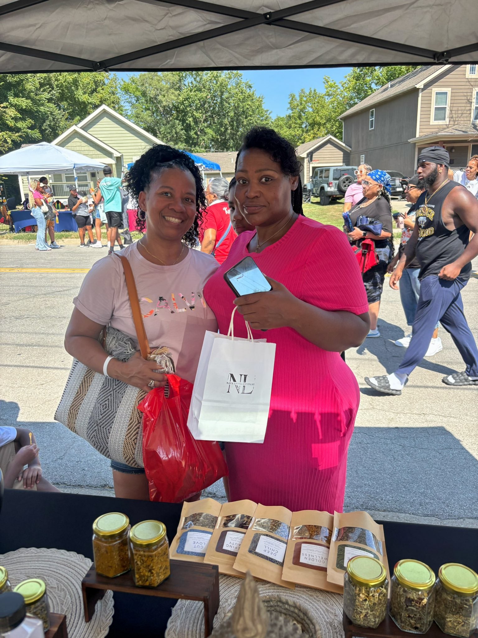 Two women standing under a Nava Living Co. tent with loose leaf tea jars and bags on a street market