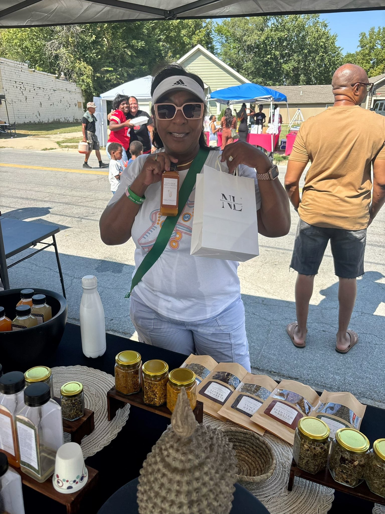 Woman holding a Nava Living Co shopping bag at an outdoor market stall with loose leaf tea products on display.