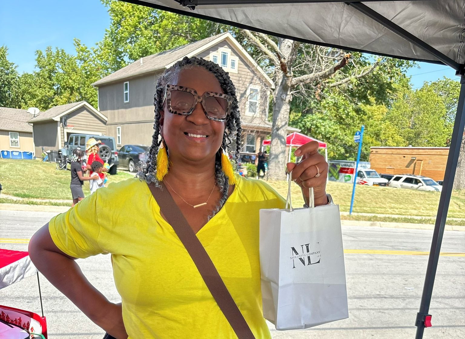 Woman in yellow shirt holding a Nava Living Co. herbal teas, standing behind a table with jars and packages filled with loose-leaf tea.