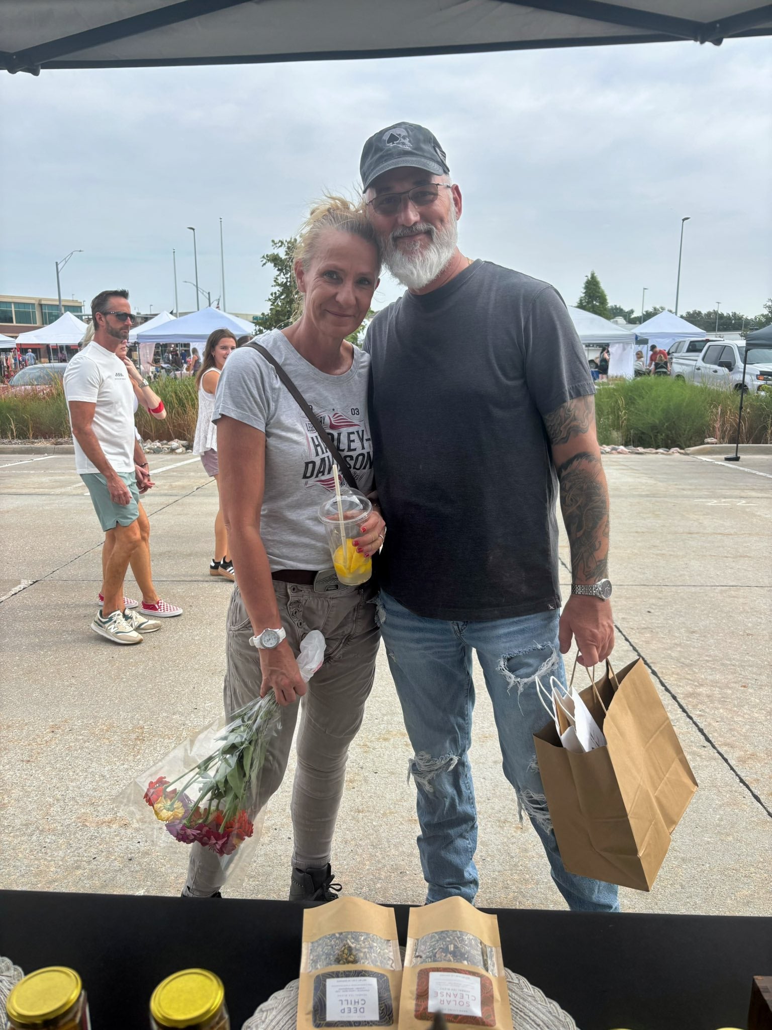 Two people standing together in a parking lot with Nava Living Co. shopping bags and produce.