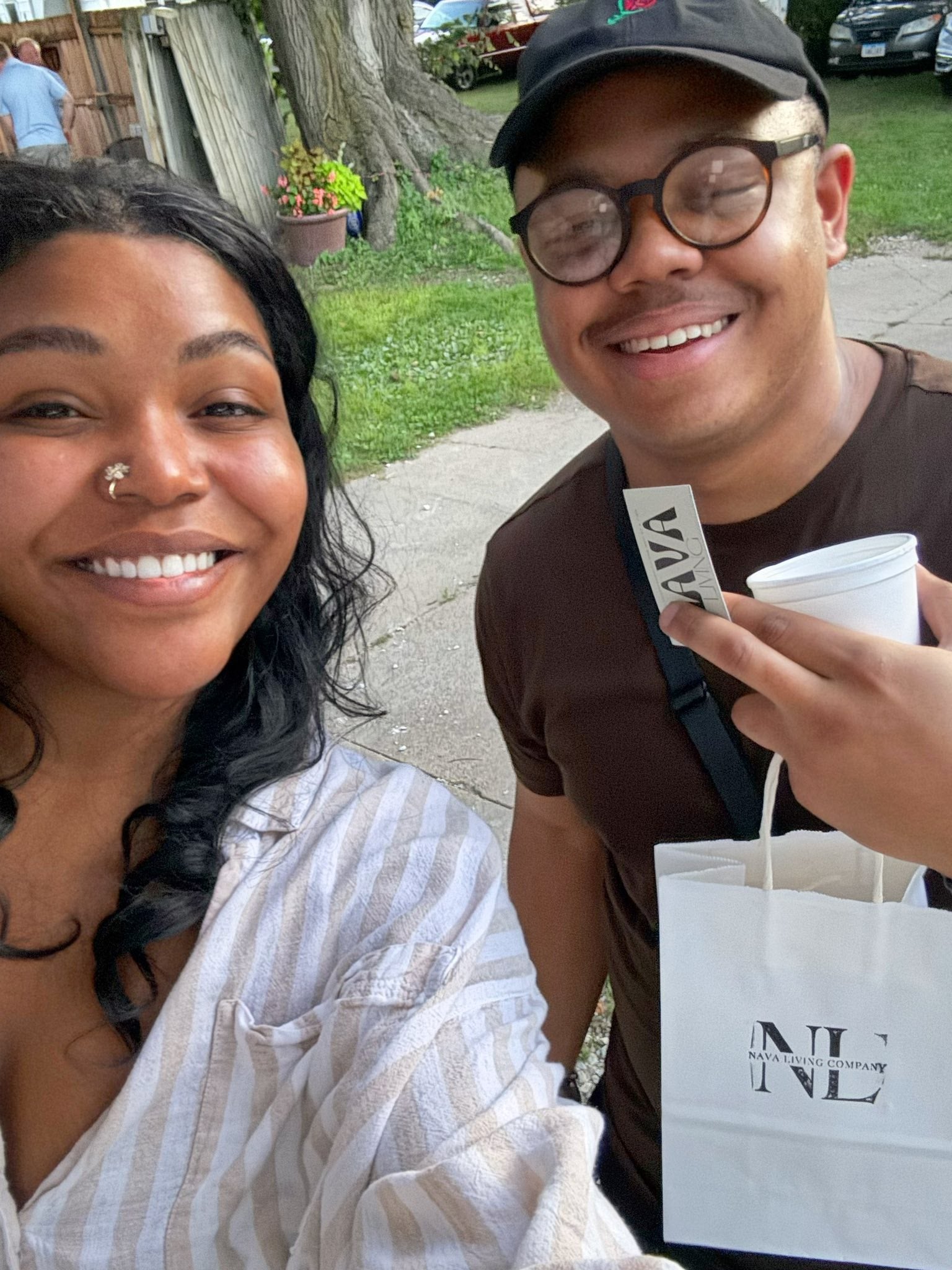 Two people smiling outdoors, one holding an herbal tea cup and a Nava Living Co bag