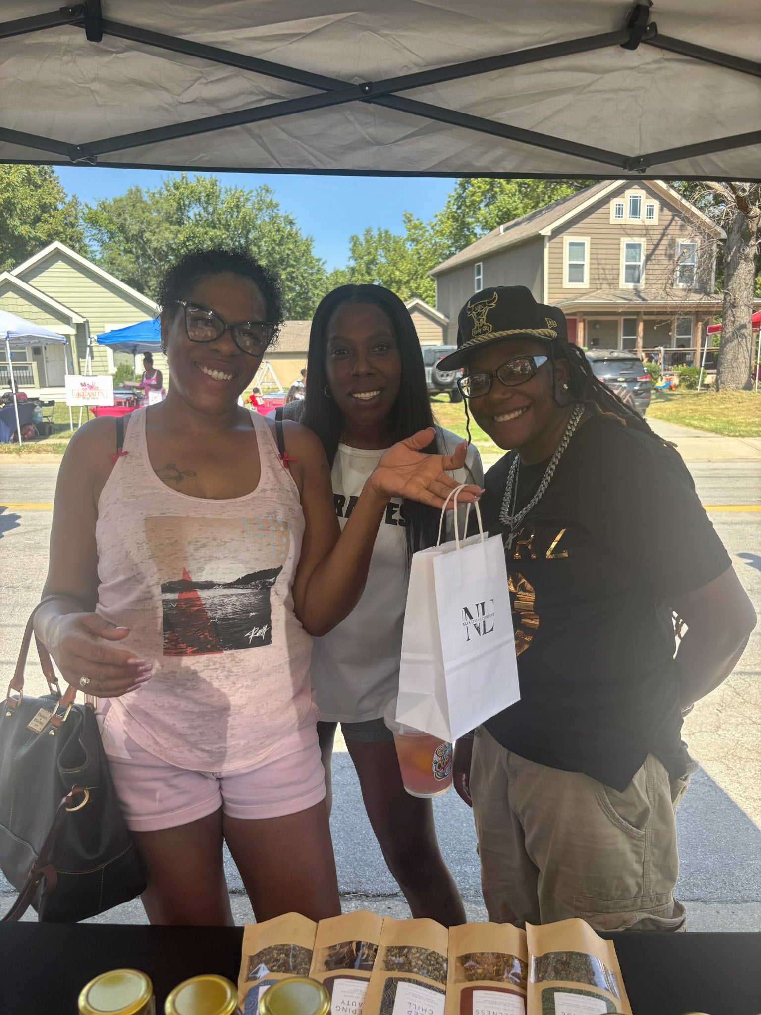 Three people standing under a Nava Living Co tent with a table displaying herbal tea blends, including a white bag.